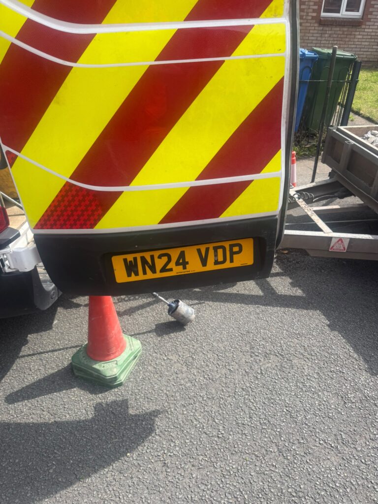 Rear of a service van with safety cone and trailer during roadside work